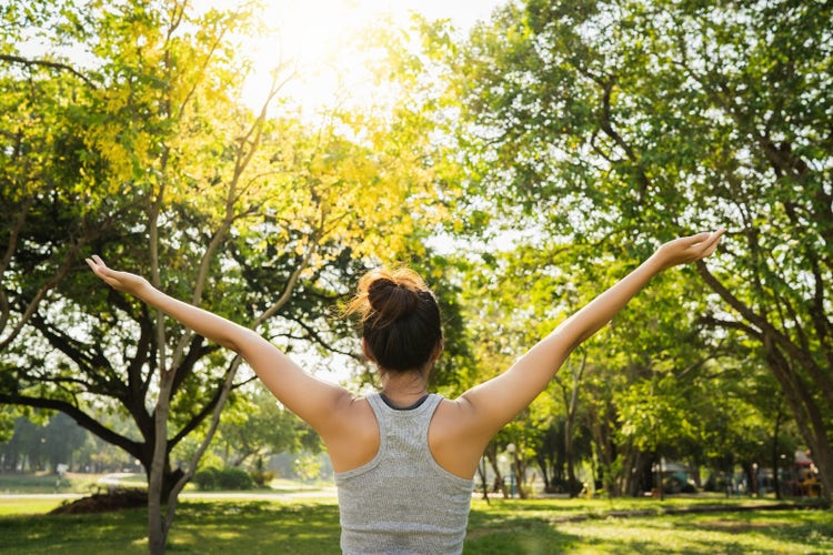 Mujer con los brazos abiertos en la naturaleza, alcanzando una salud mental positiva y bienestar emocional.