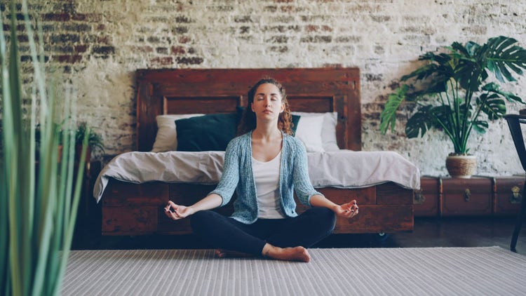Mujer meditando en su habitación, practicando el autocuidado emocional y la salud mental preventiva.